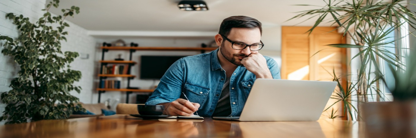 Man holds pen to paper while looking at computer.