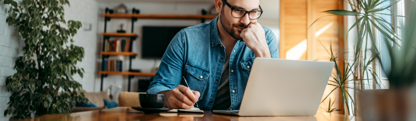 Man holds pen to paper while looking at his computer.